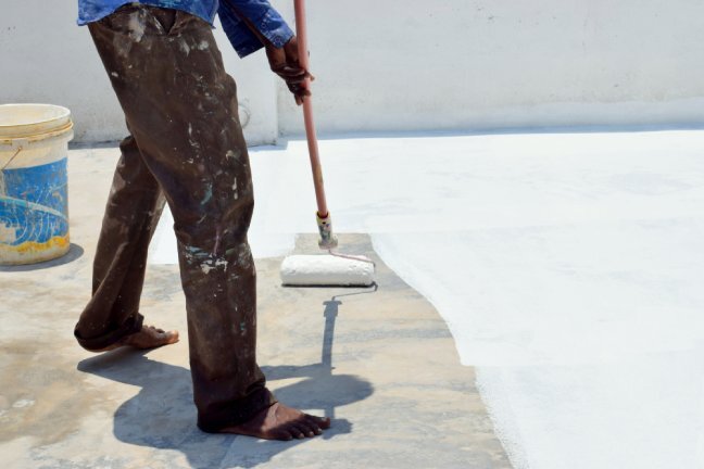 Person painting roof white with roller.