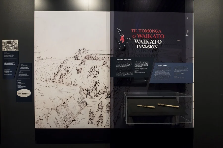 A Museum display about the Waikato invasion. There is Māori and English text on the right, and on the left is a large diagram of British attack on the Māori pā from the trenches below.