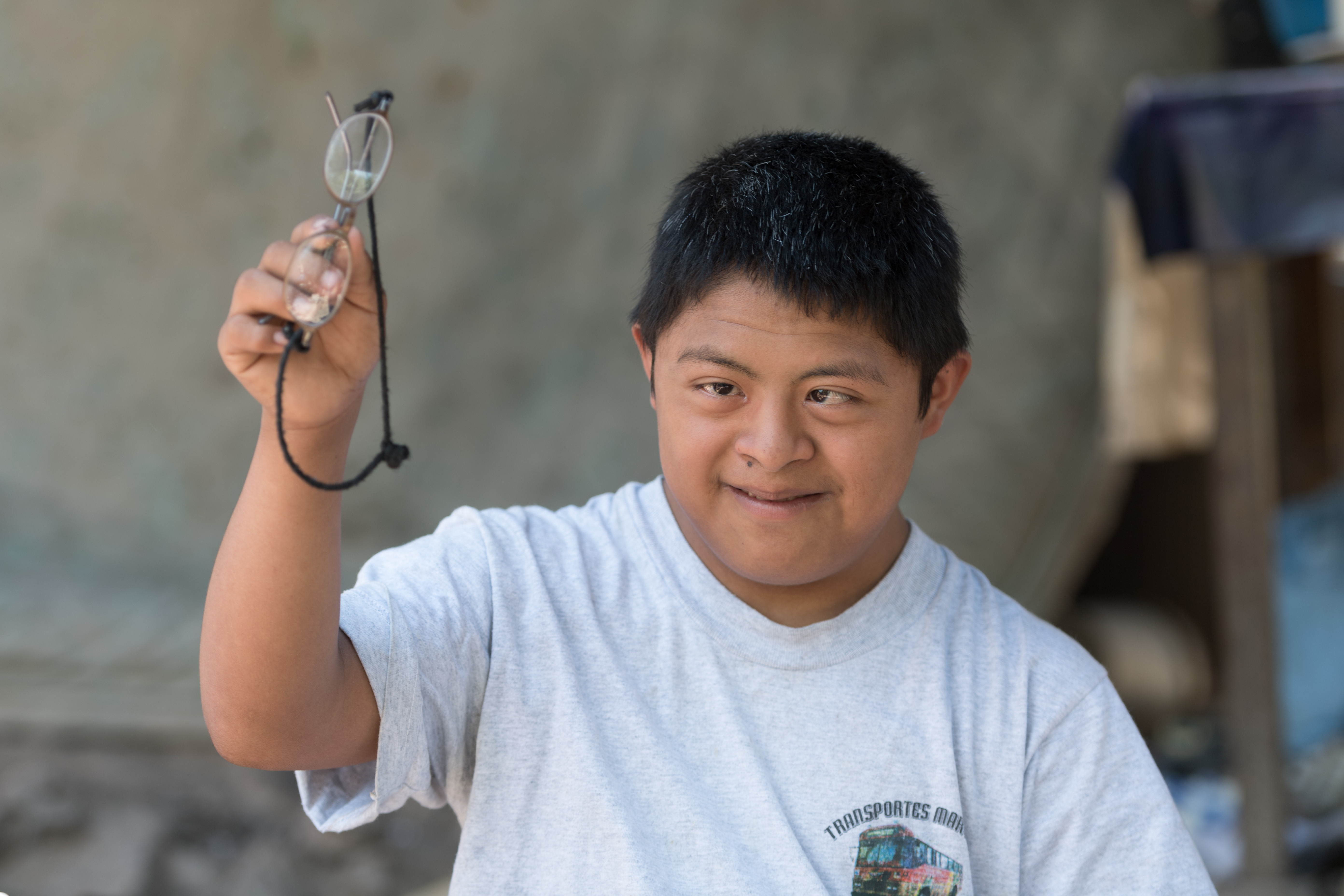 A teenager with Down syndrome holding up his glasses