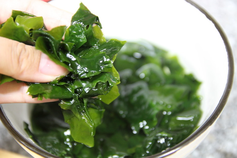 glass bowl containing wet green leaves and close-up of a hand holding some