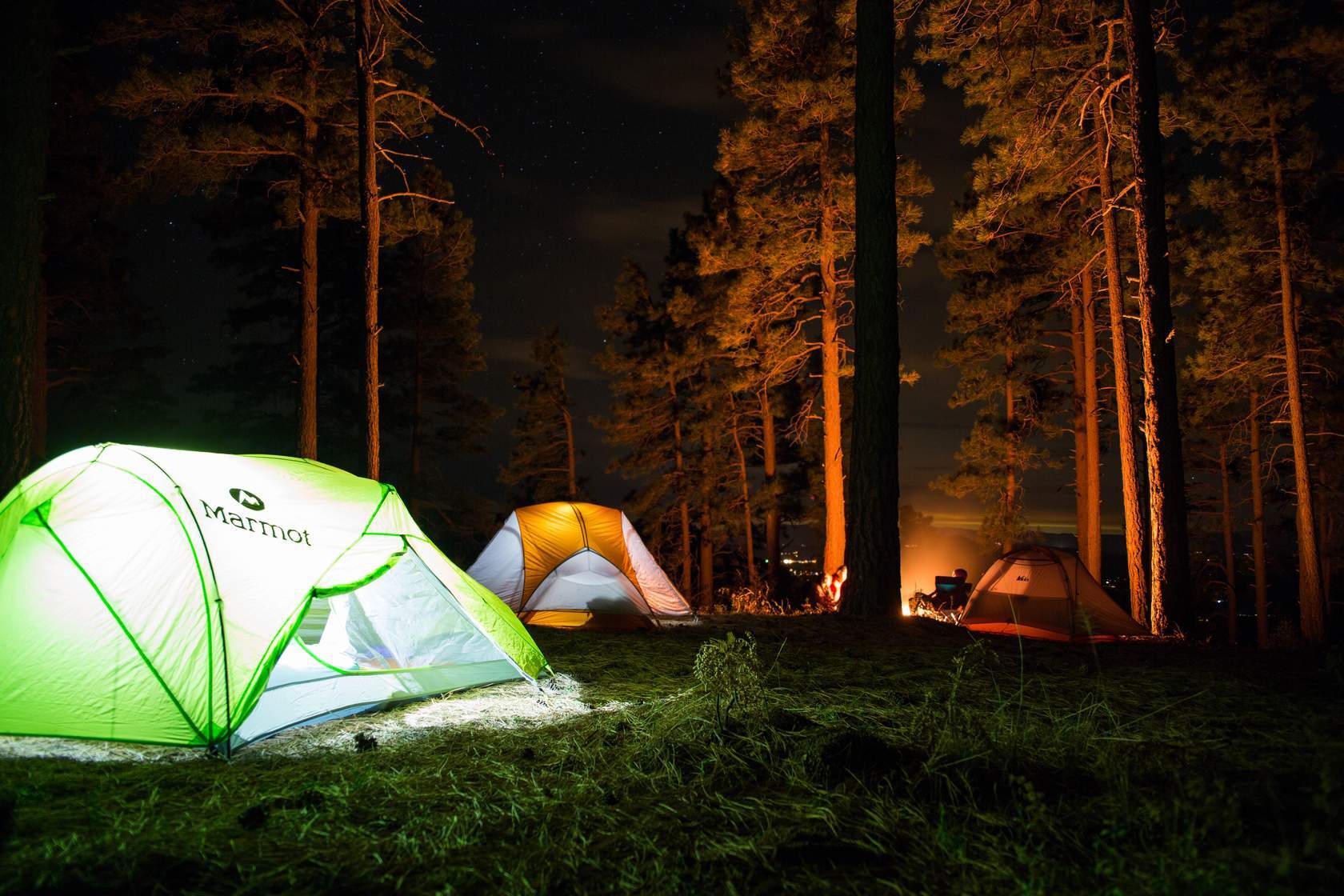 Three illuminated tents in a forest at night