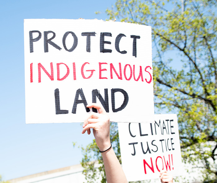 Protestors holding up signs: "Protect Indigenous Land" and "Climate Justice Now!".