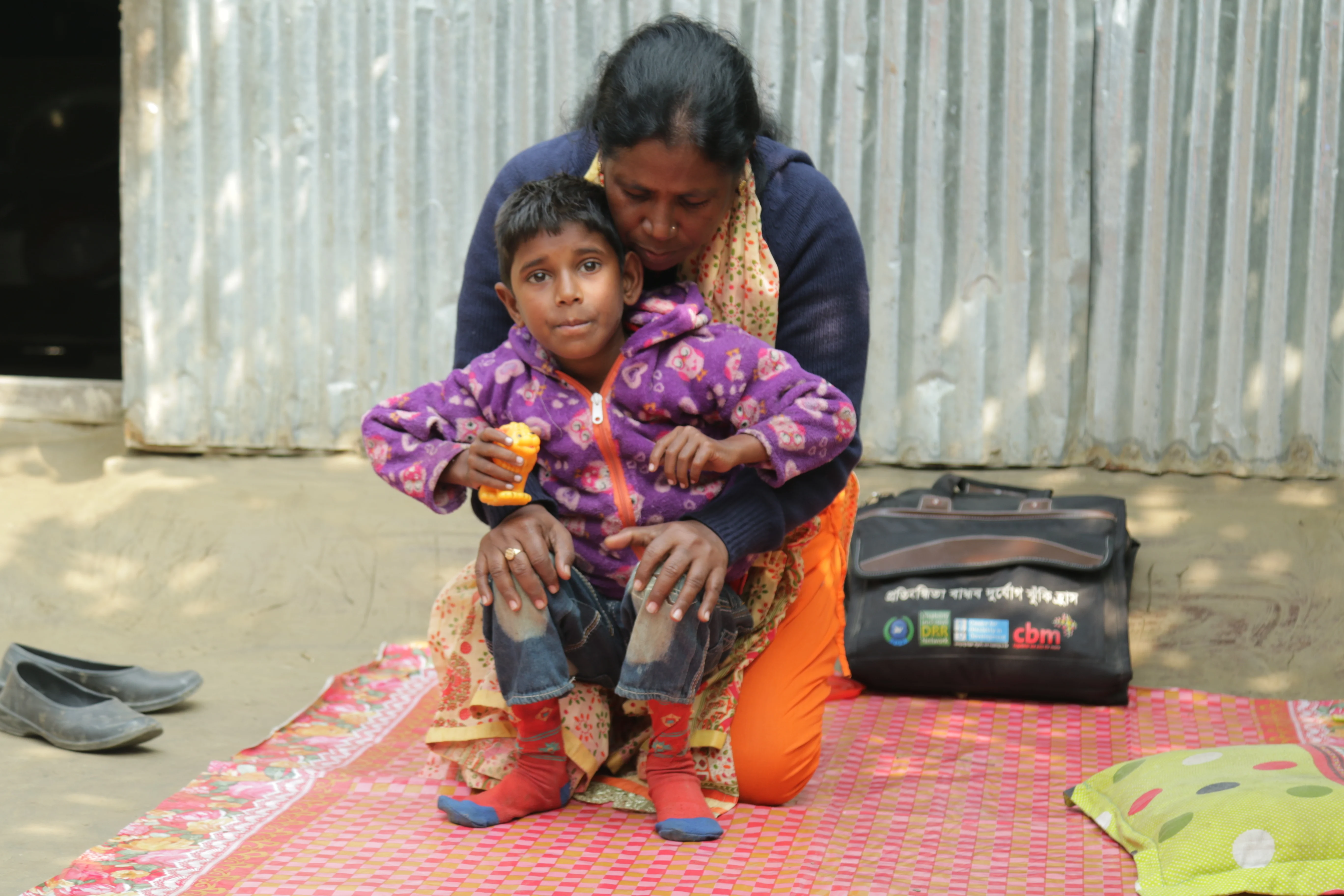 A boy being supported through physiotherapy. He is sitting on the therapist's knees.