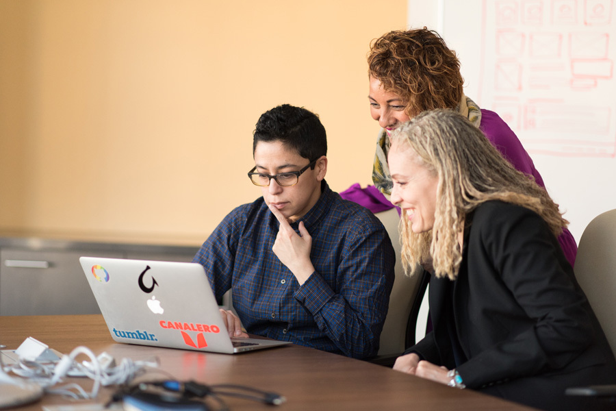 Three women beside a table looking at a laptop