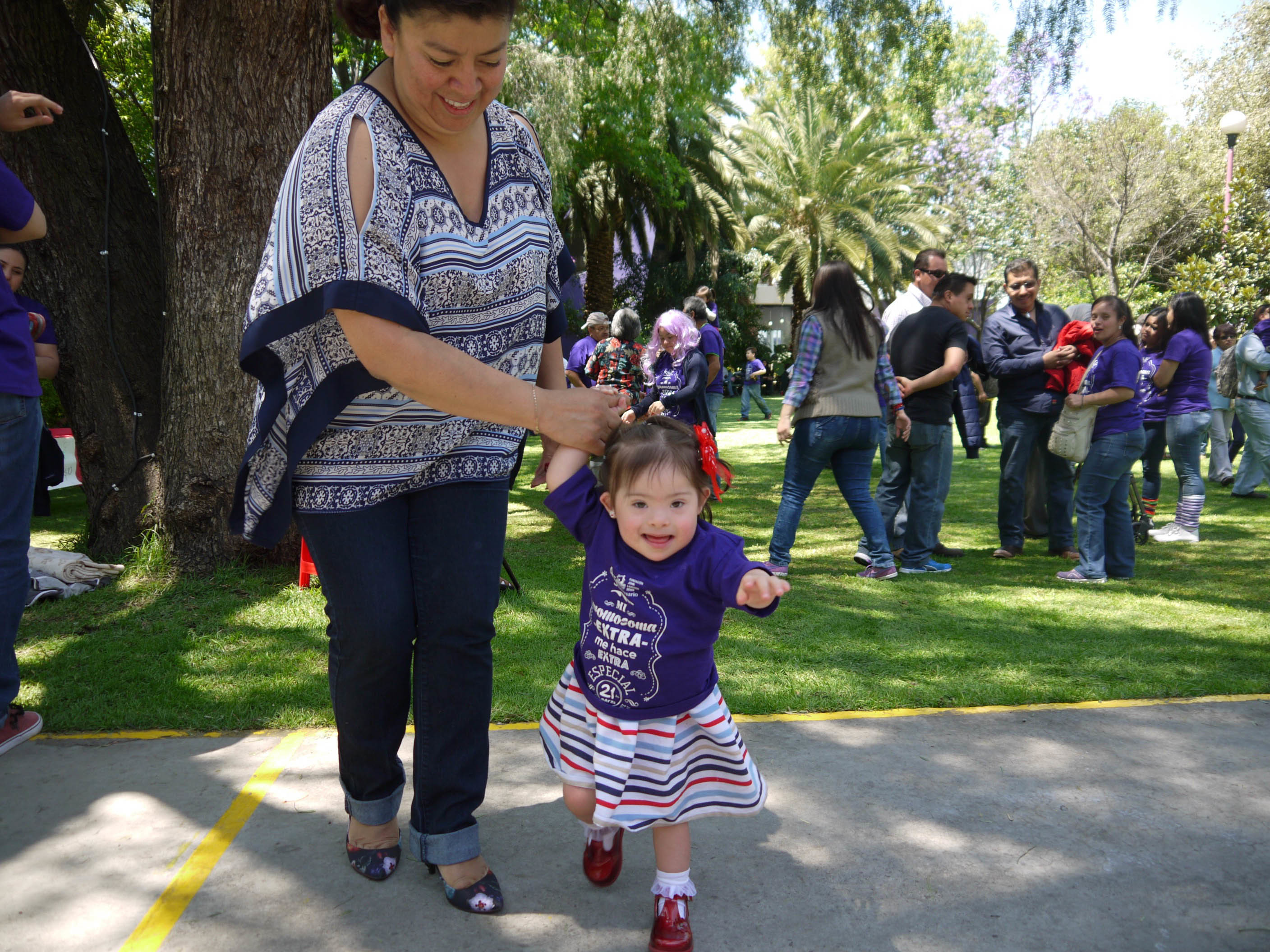 A young girl with Down syndrome holding the hand of a relative as they walk along.