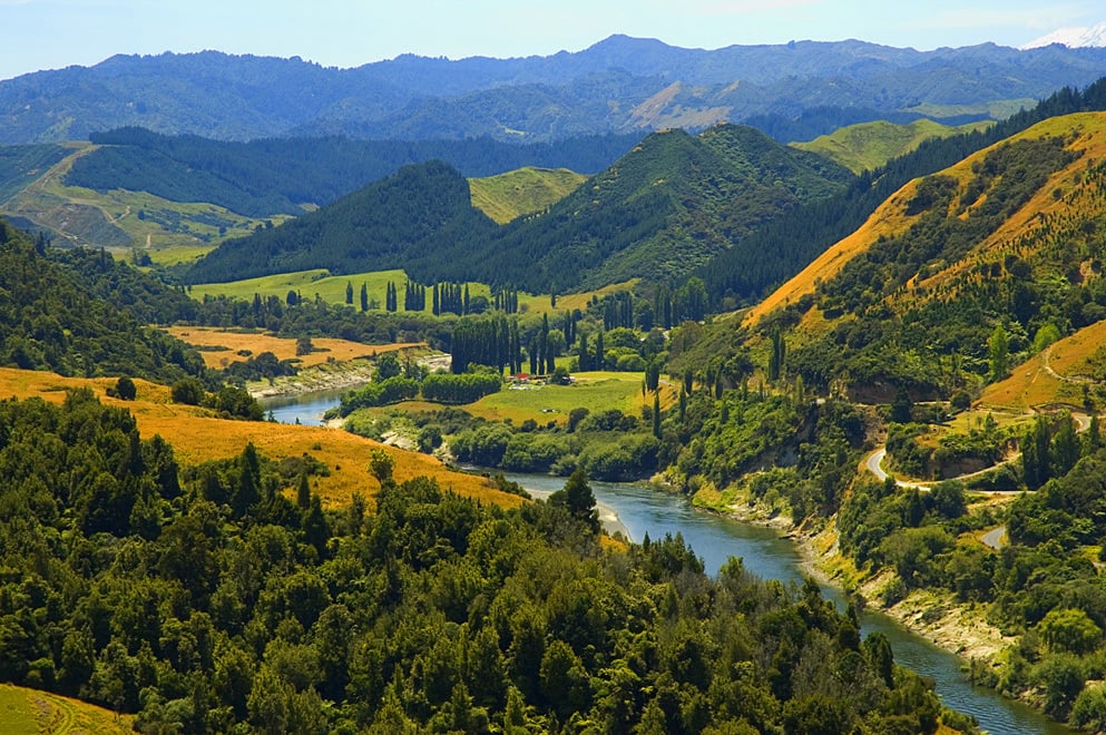 a blue river snakes through a valley surrounded by hills covered in green and yellow bush.