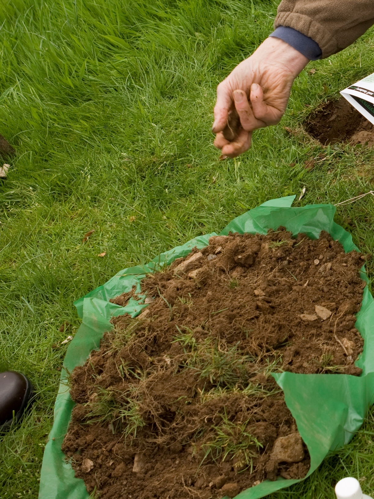 Freshly dug soil, on a piece of green polythene, with a hand crumbling it