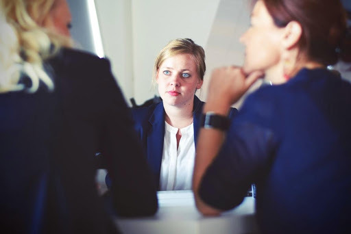 Colour photograph showing three women, one facing the camera and two with backs to the camera in what appears to be a business meeting