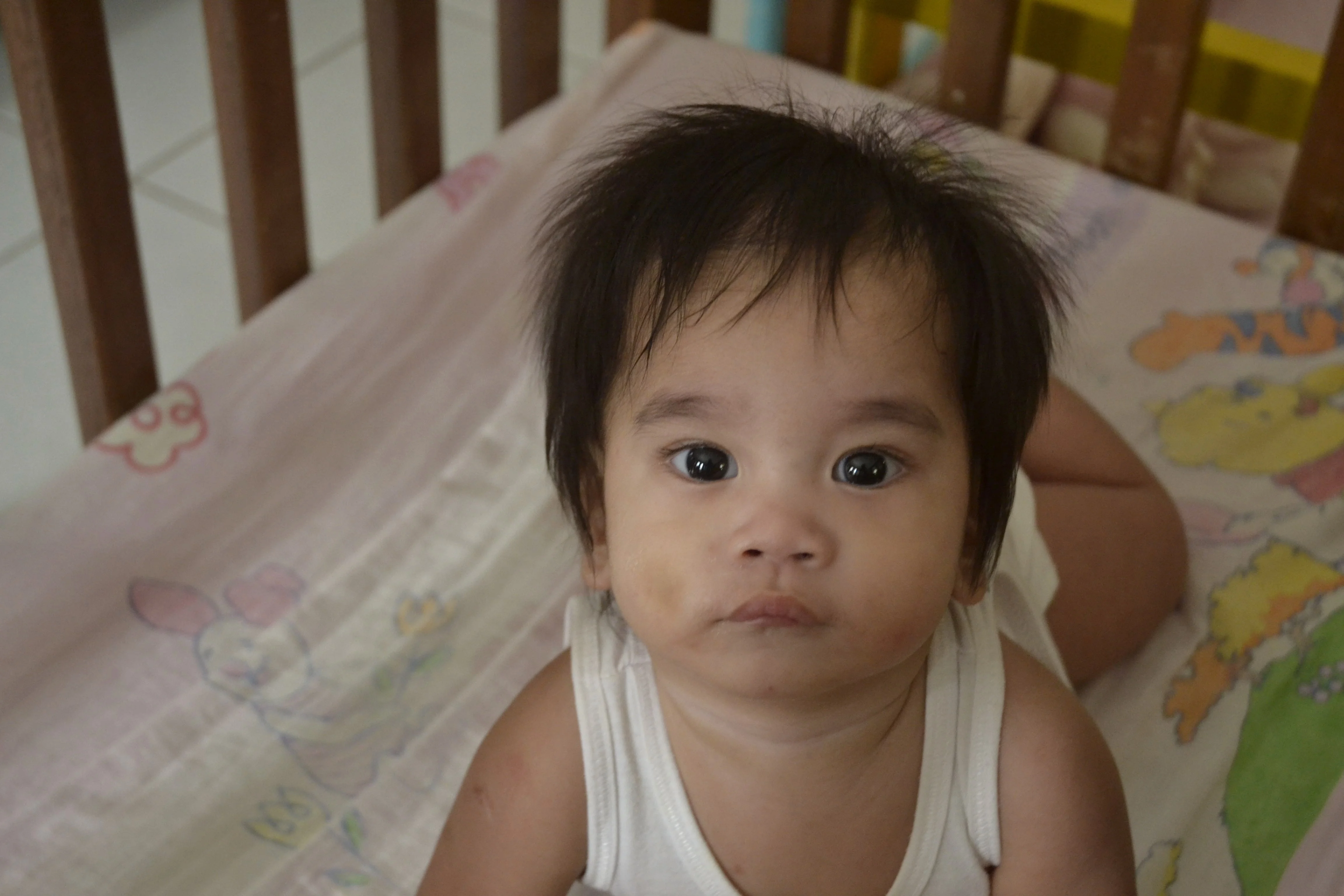 A young child is lying down in a cot.