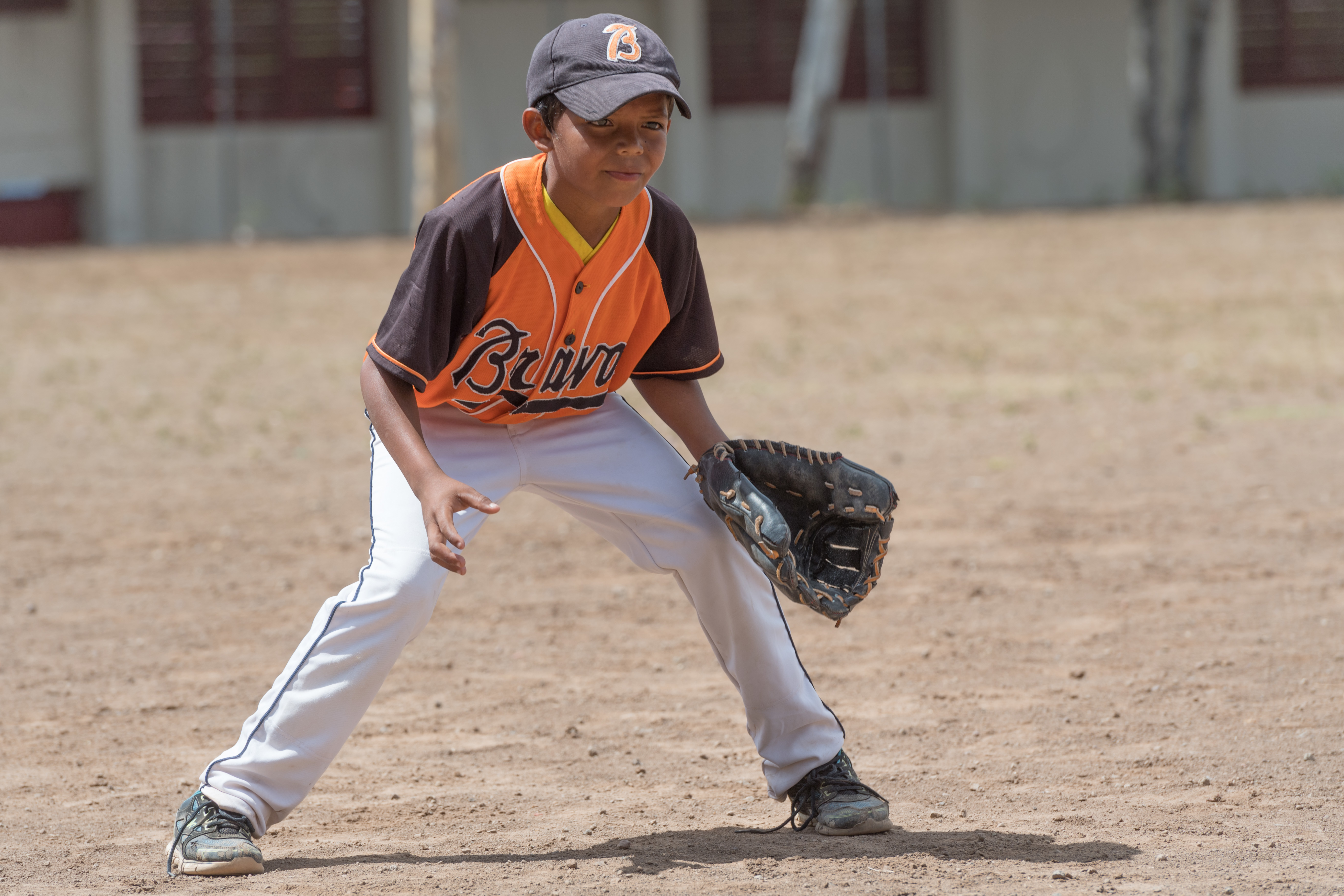 A young adolescent boy is in a baseball kit, including a baseball glove and baseball cap. He is crouched down waiting to receive the ball.