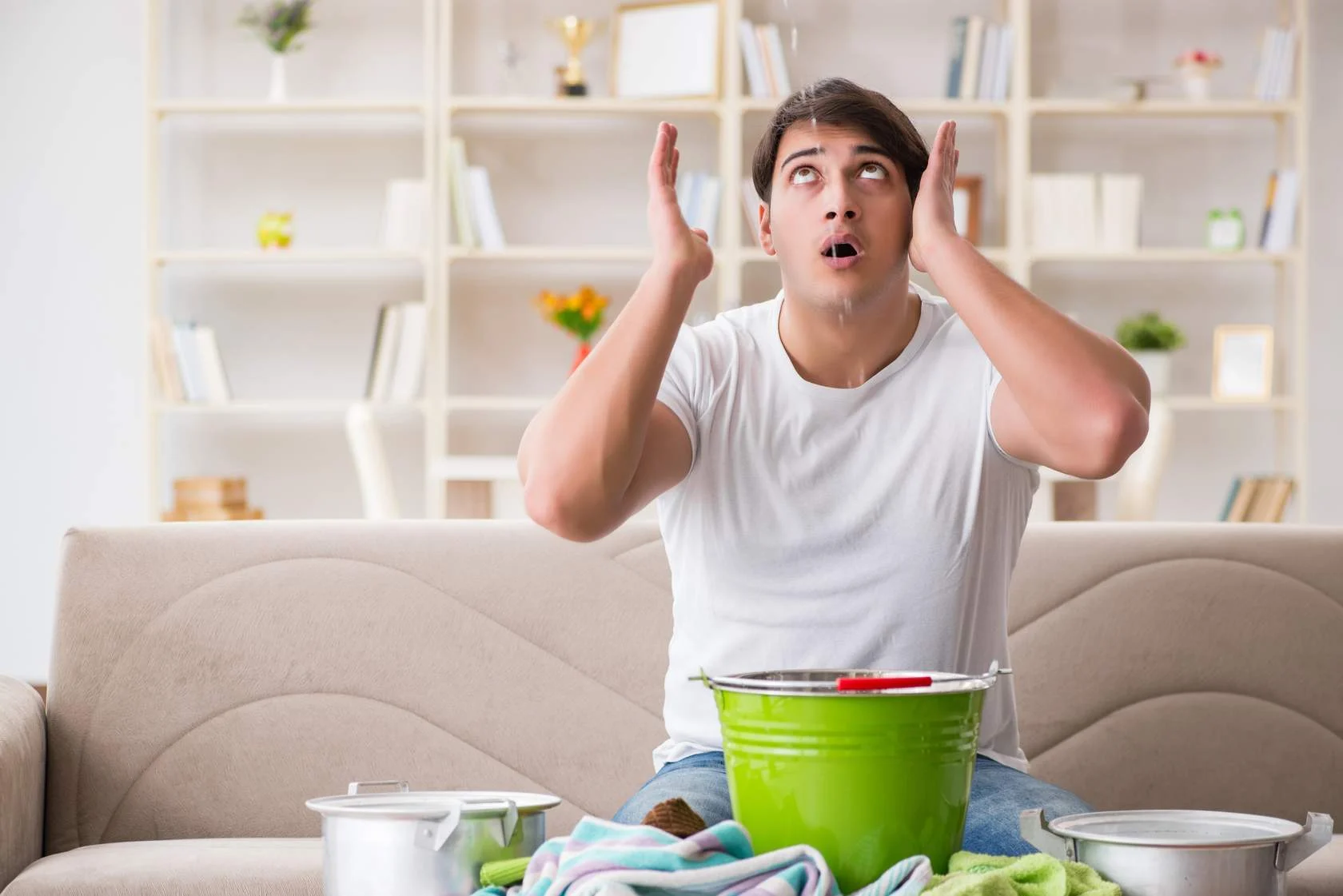 Man looks up as water drips from above into bucket in front of him