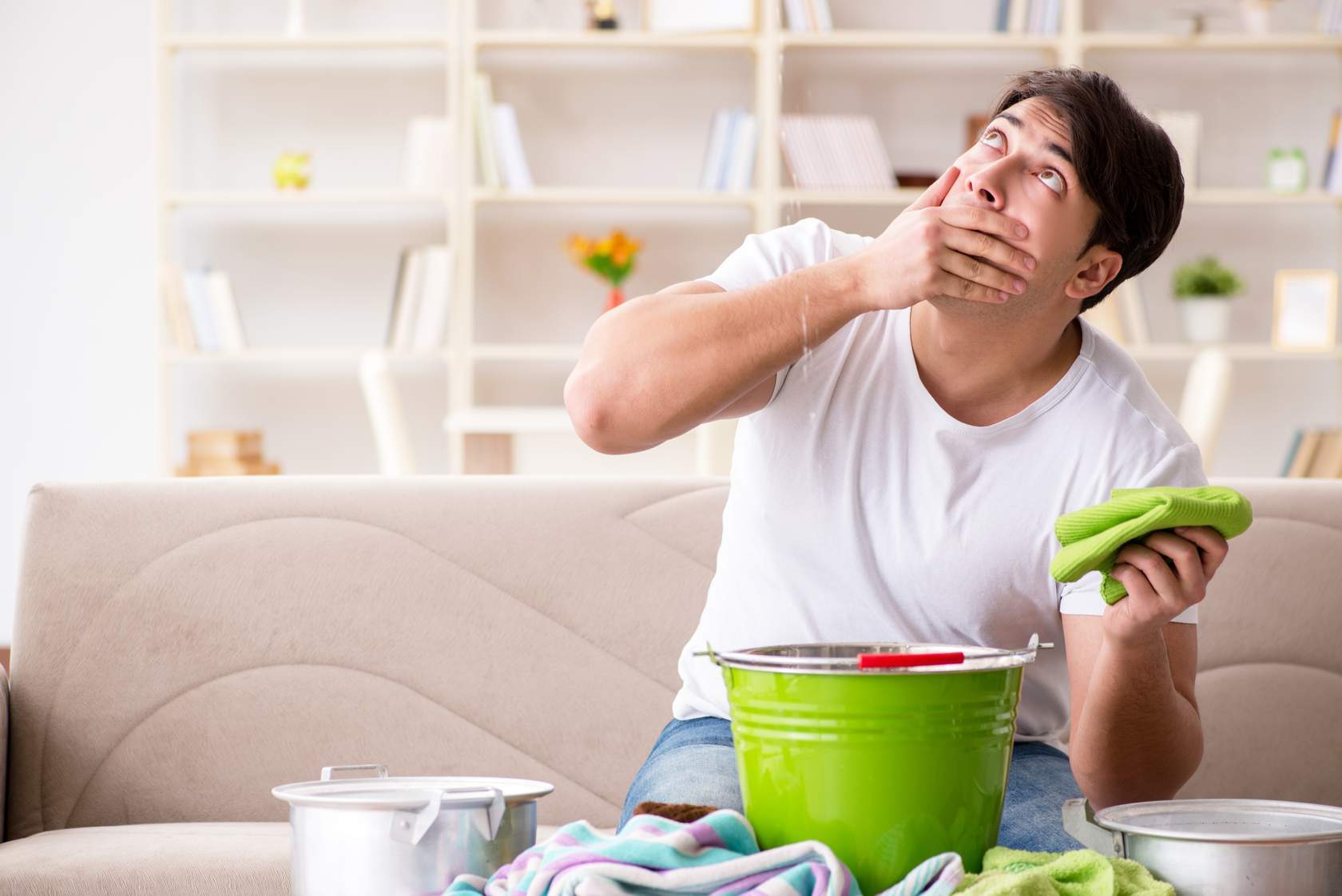 Man looks at ceiling with bucket to catch drips