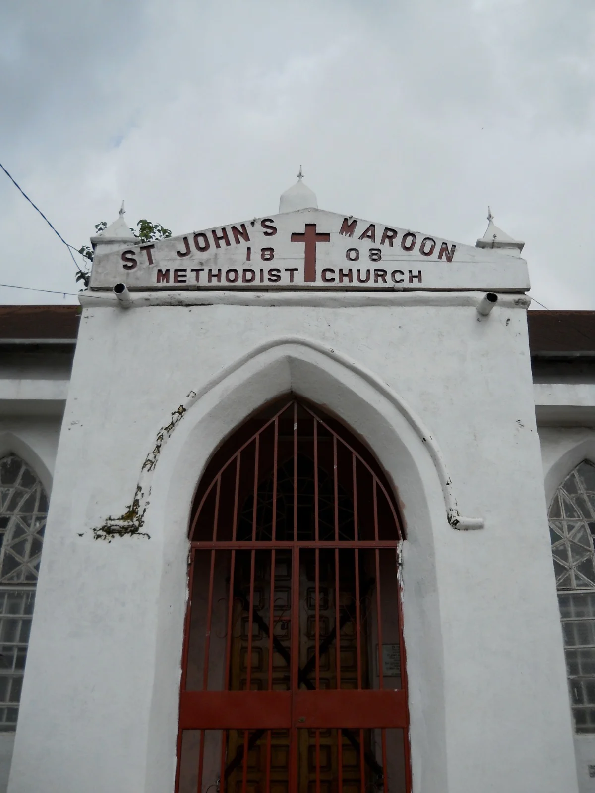 White church front with a sign in red paint which reads, St John's Maroon Methodist Church, 1808