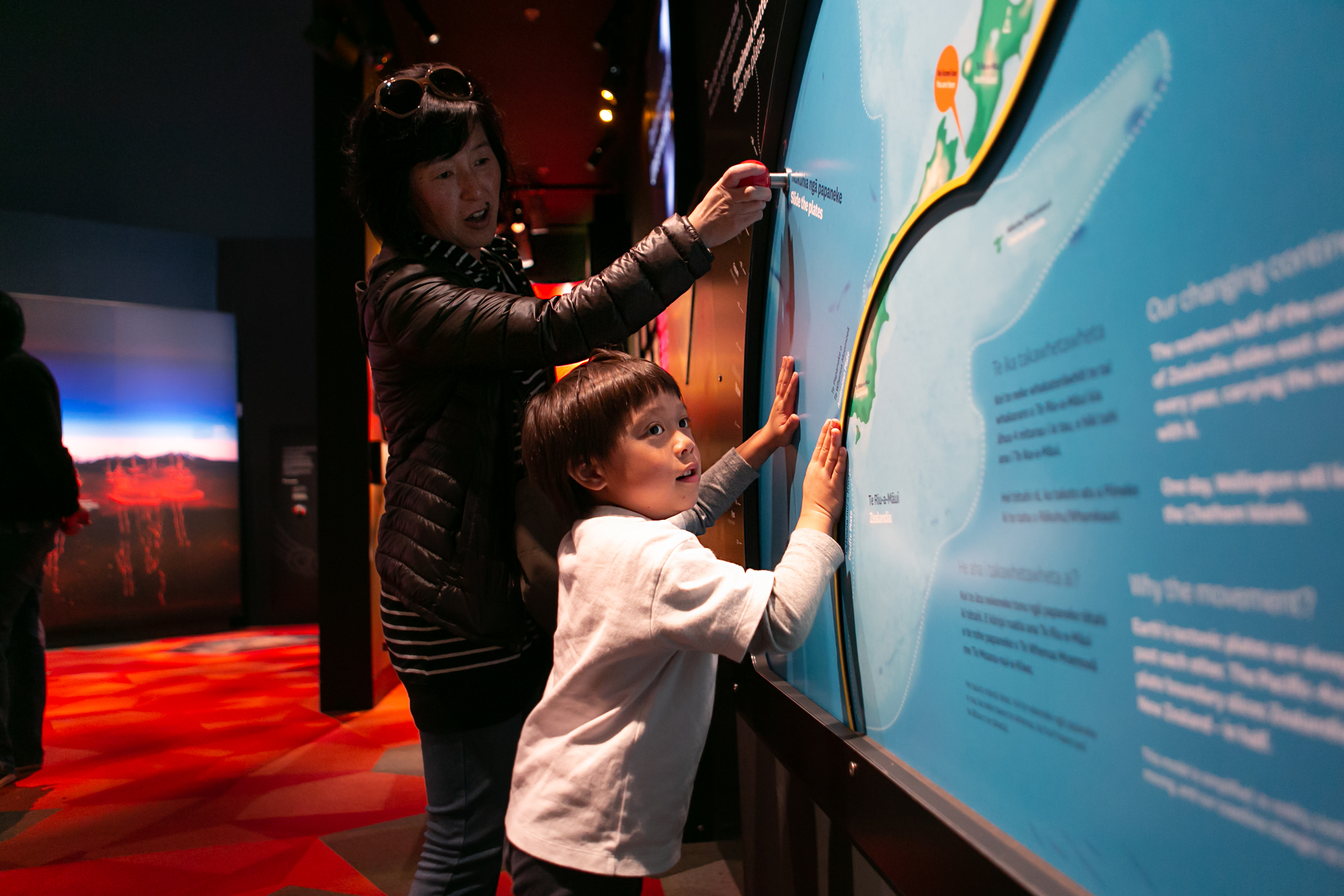 A girl of around 3 years old plays with an interactive display of New Zealand's plate tectonics as her mother looks on