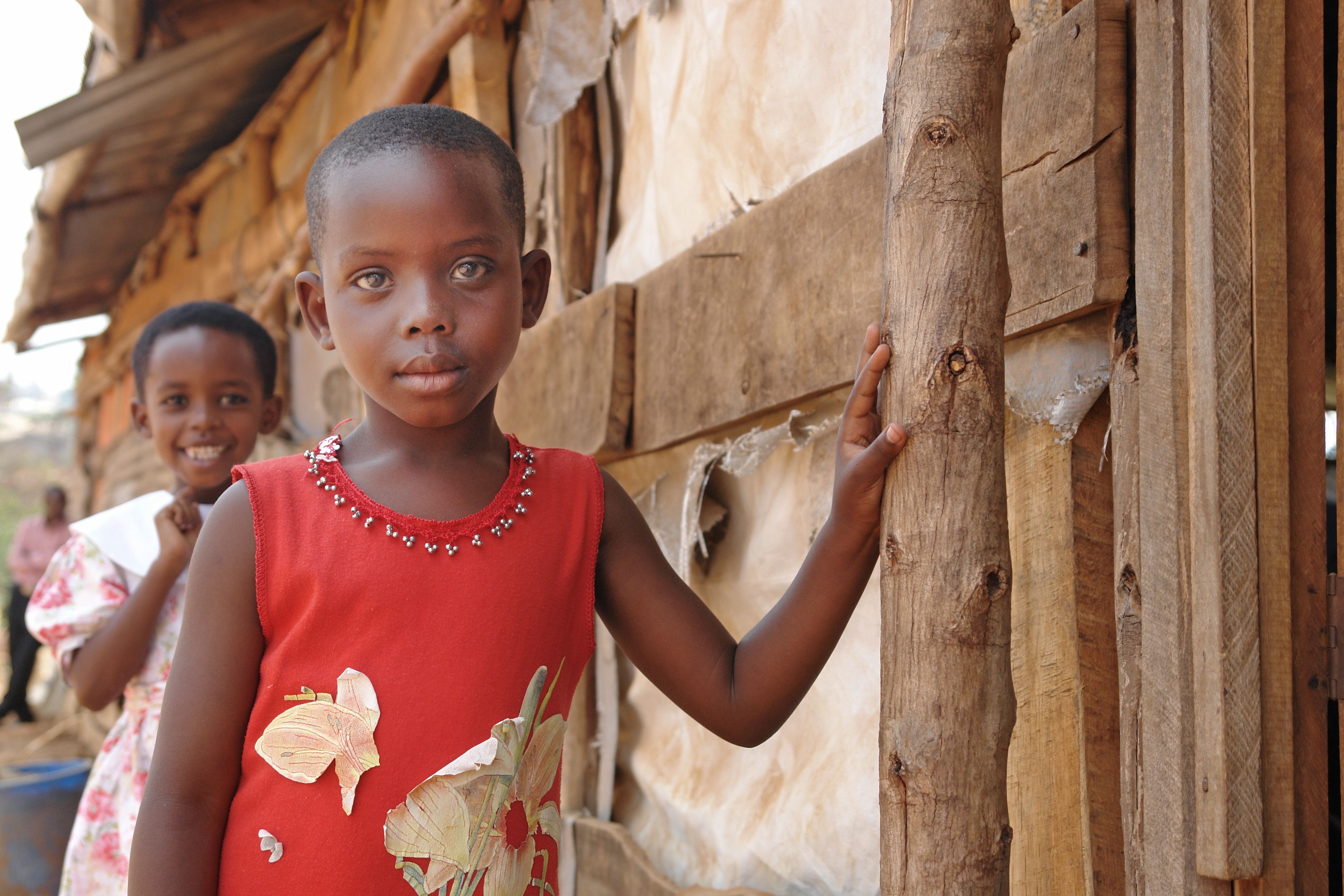 A young girl leans an arm against a wooden building and looks into the camera