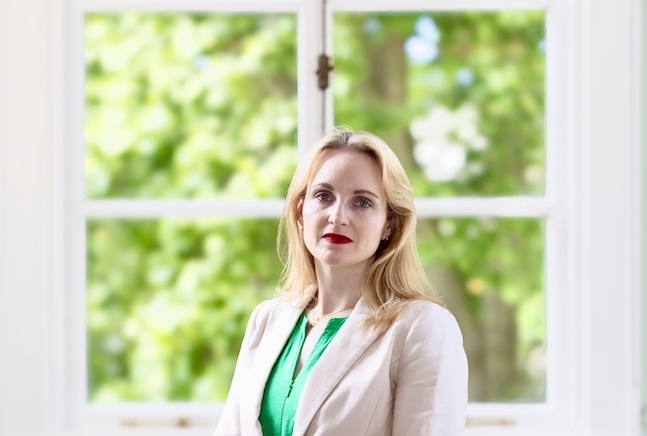 Photo of Dr Beth Malory stood in front of a window with a view of trees.