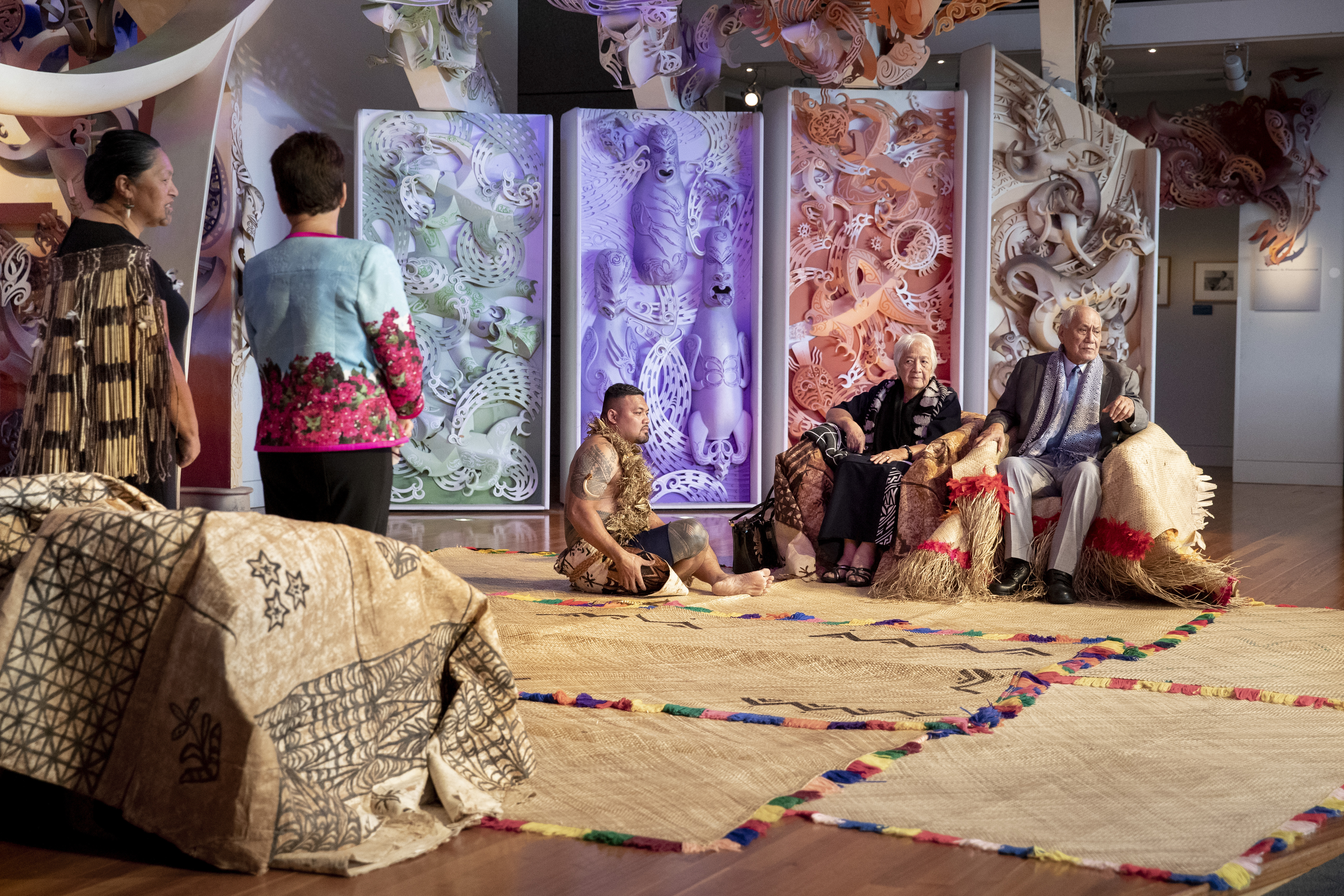 The presentation of several precious tapa cloth to a seated man and woman in Rongomaraeroa. They are dressed in ceremonial Pacific Island dress that signifies they are important people.