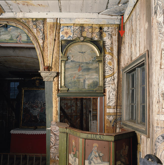 A picture showing the interior of a Stave Church showing a pulpit. A red arrow indicates a corner post.