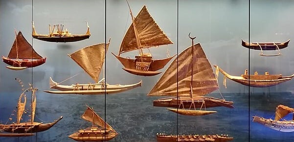 a display of various model pacific canoes. They vary in size and hulls, some have sails.