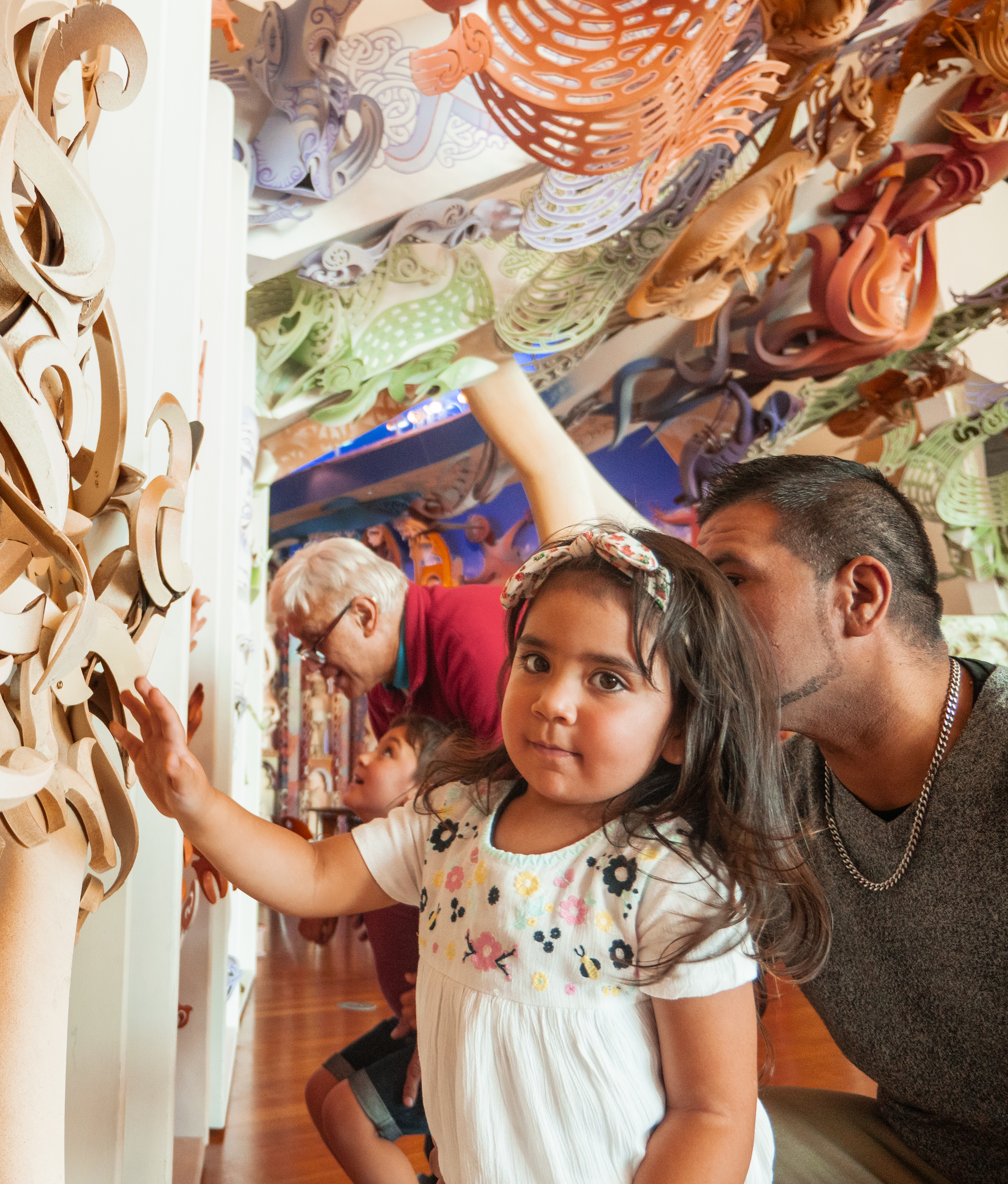 A Māori father and daughter touch the carvings in appreciation. She looks into the camera.