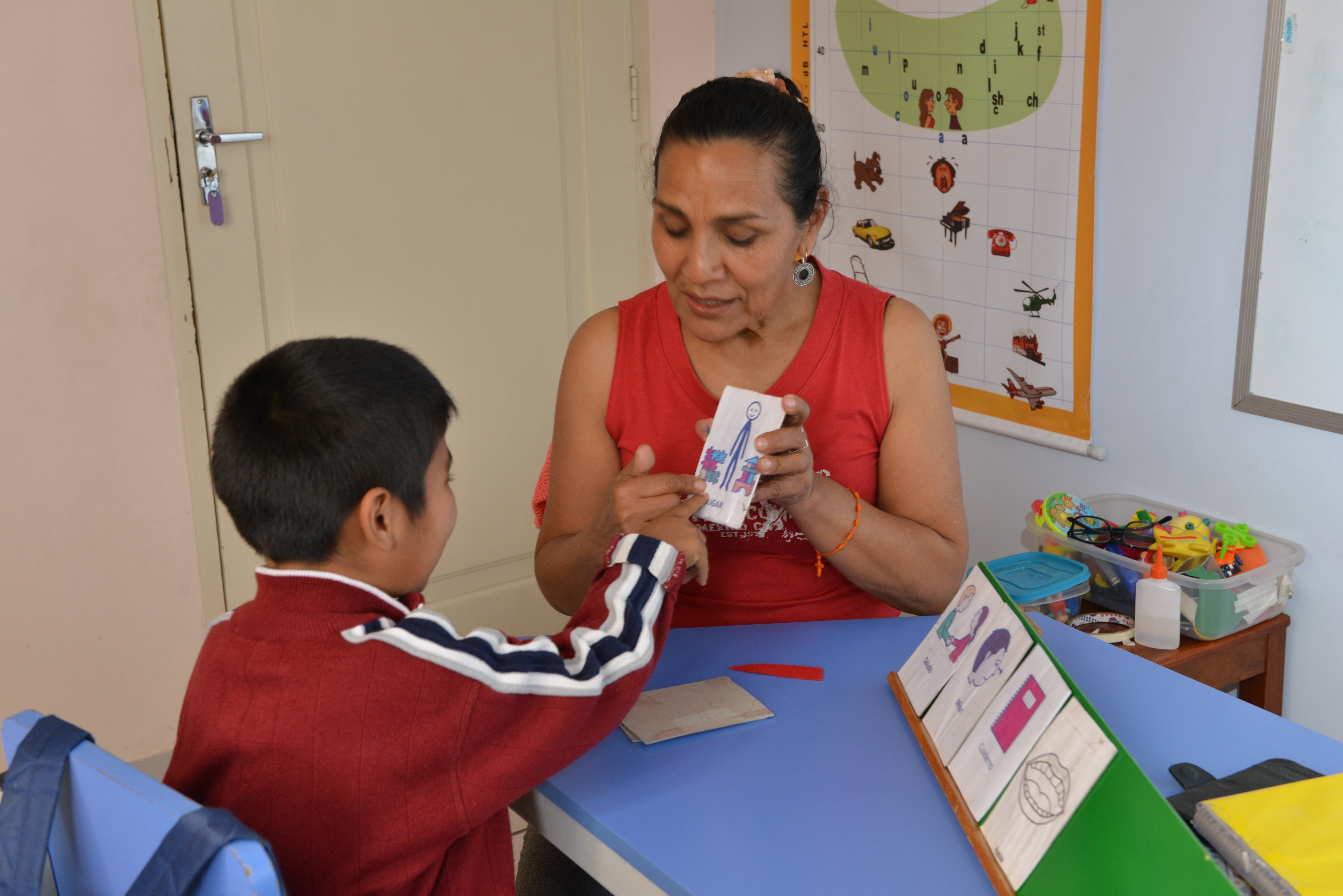 A boy is pointing at a picture card being held up by a woman.