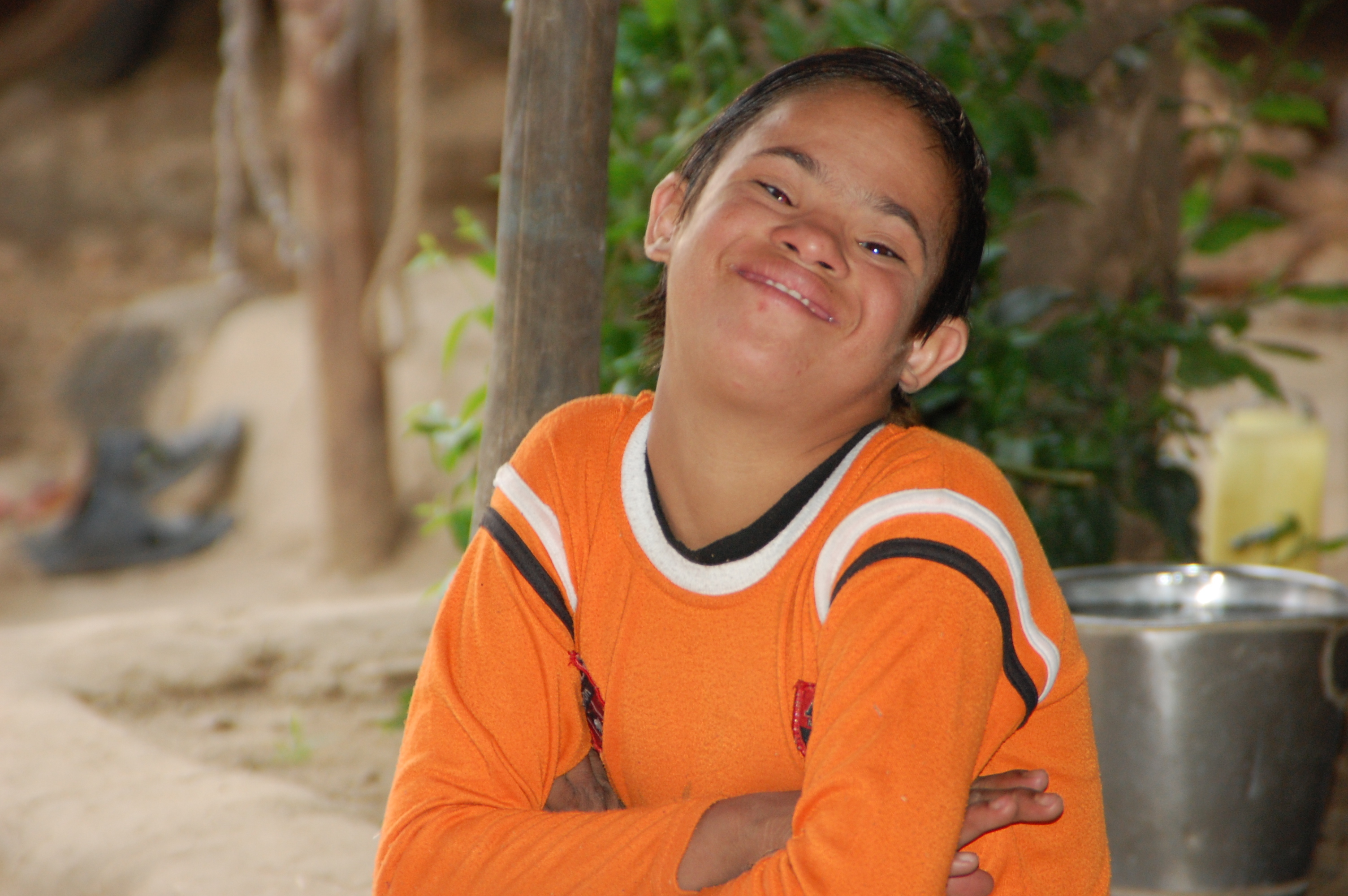 A boy with Down syndrome has his arms crossed and is smiling at the camera.