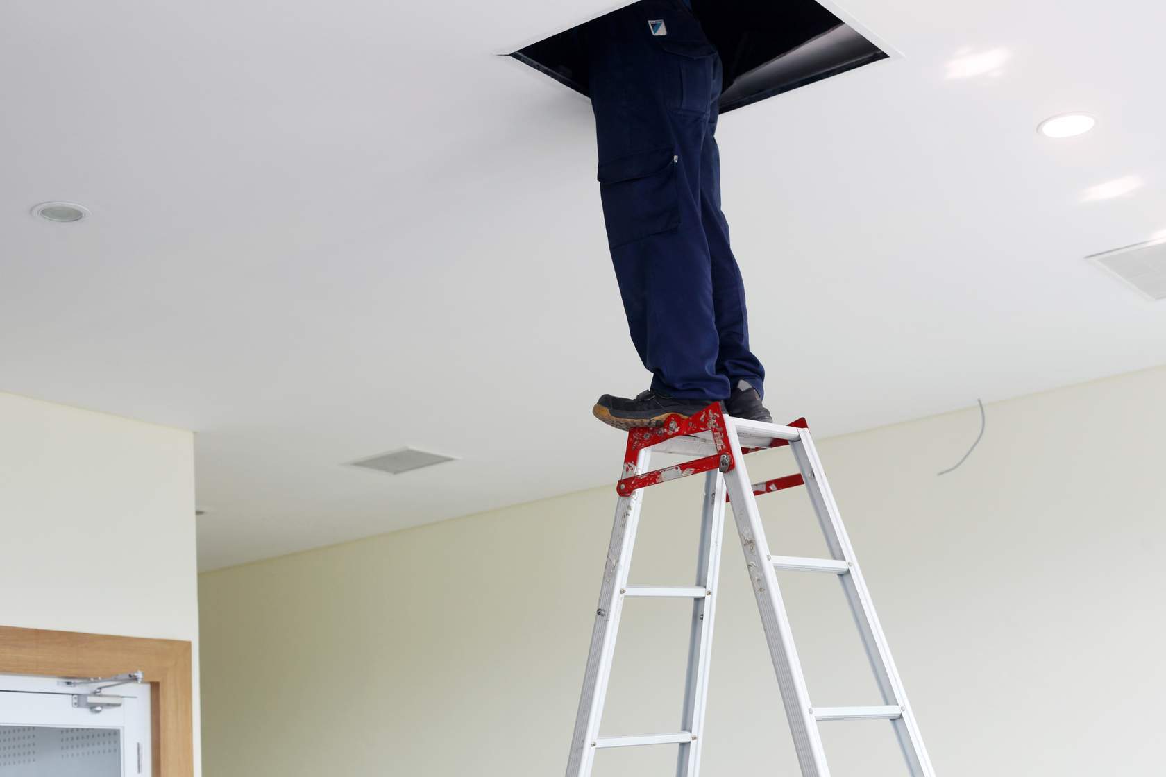 Legs standing on top of stepladder as person looks through attic hatch