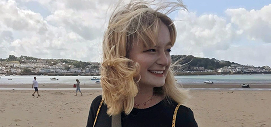 A portrait of a women with shoulder length blond hair standing on a beach