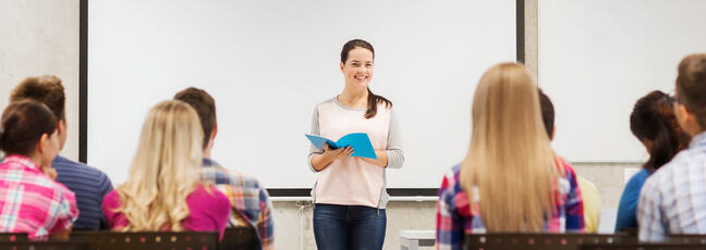 A student standing in front of a classroom of students and reading from her book.