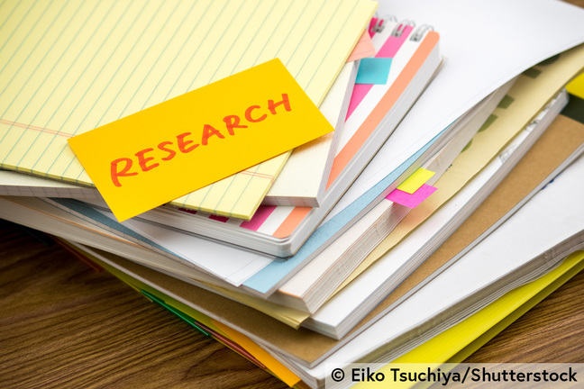 A pile of notebooks and a piece of paper on which the word 'research' is written