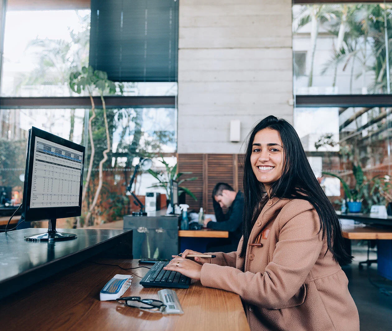 A woman sits at her desk, in a office, smiling. 