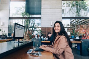 A woman sits at her desk, in a office, smiling. 