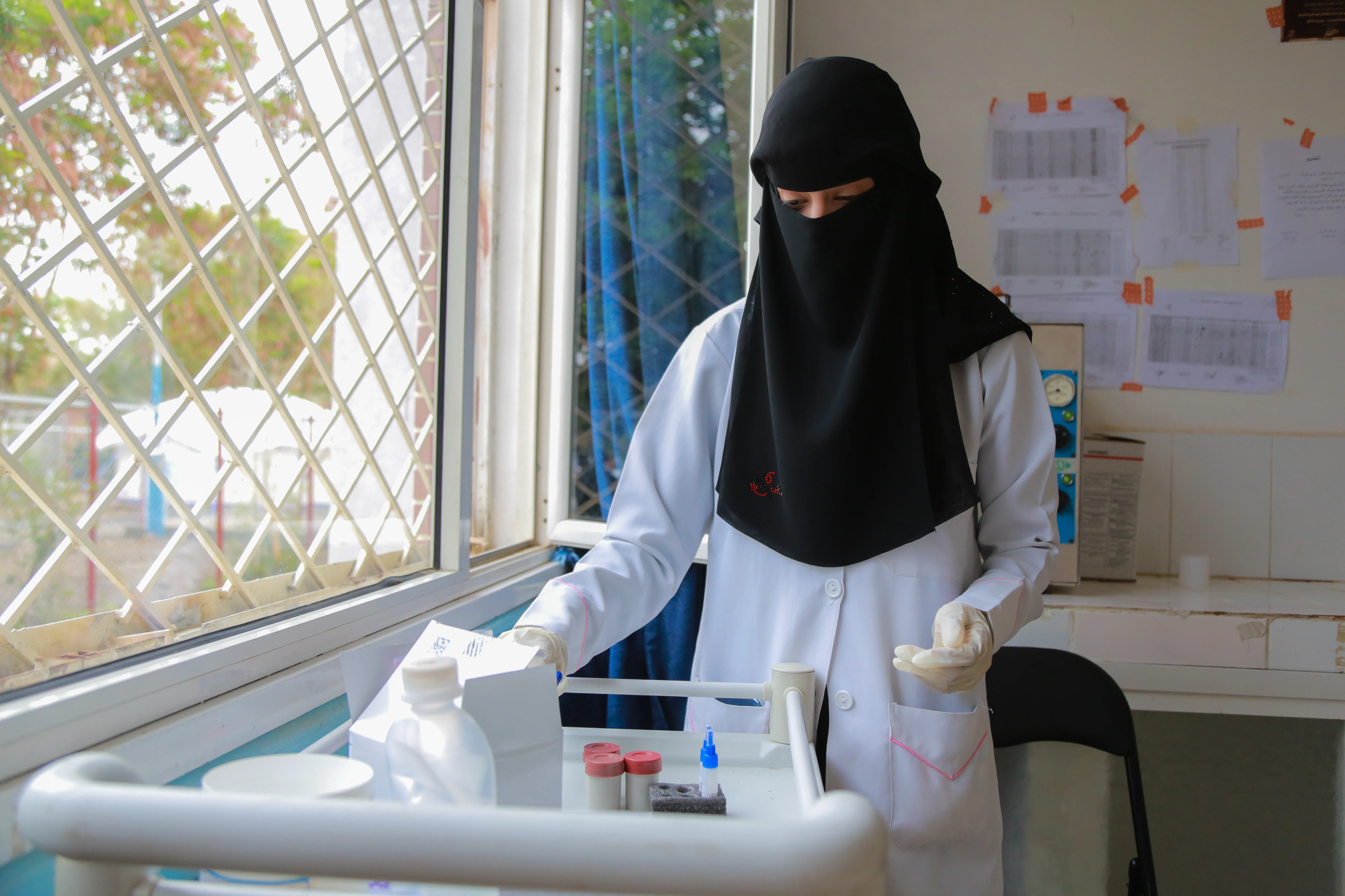 A nurse wearing gloves stands at a medicine cart sorting through various medications.