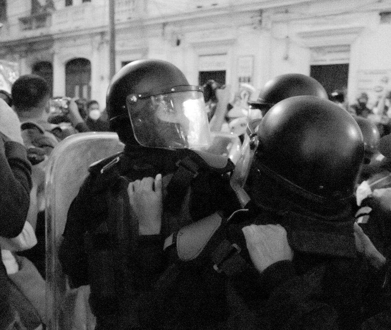 Group of police officers in full riot gear leading through a crowd of people in masks