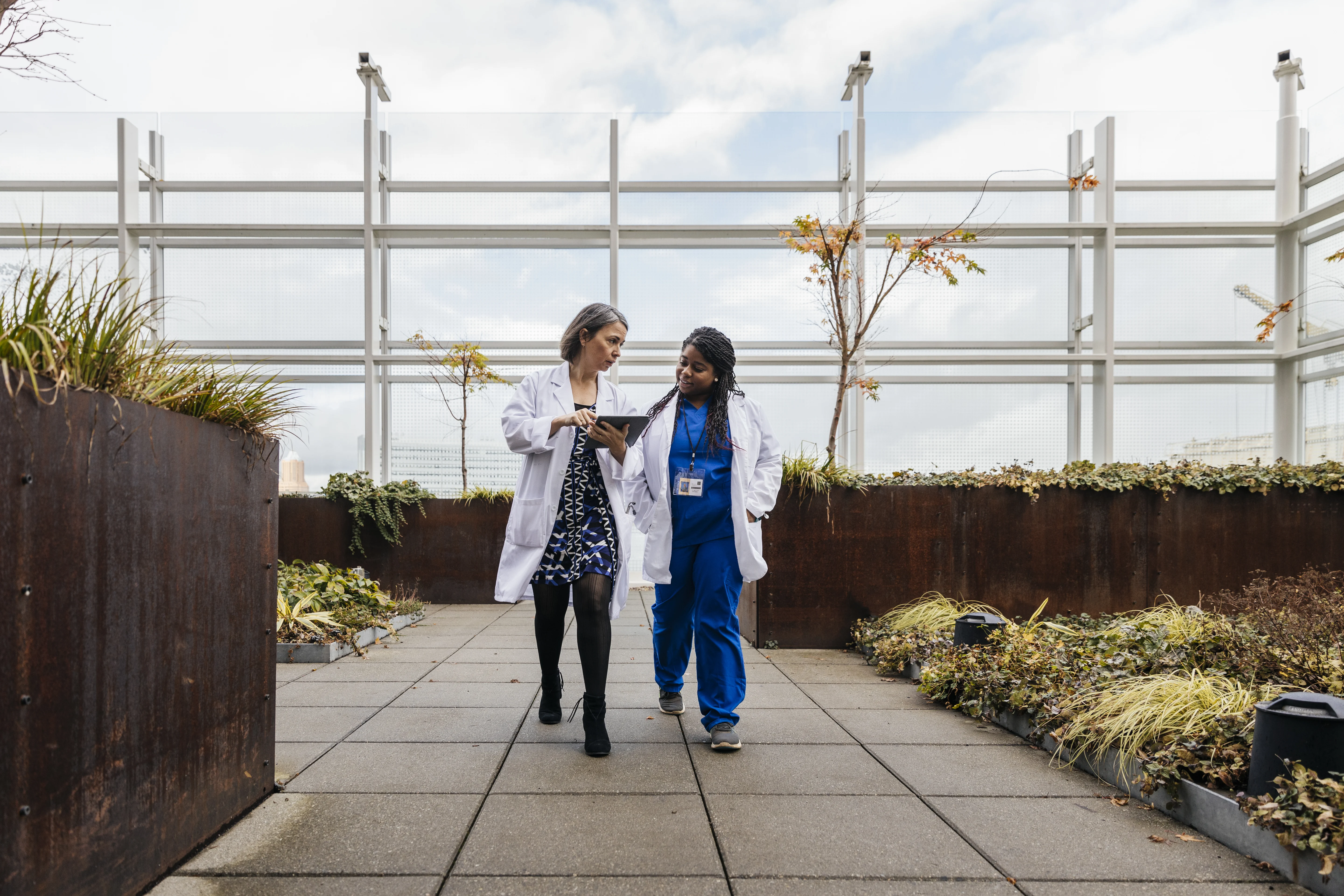 Female doctors talking while walking on rooftop of hospital.