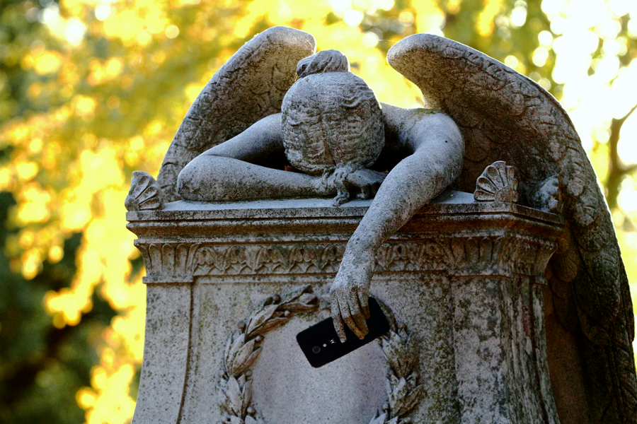 A monumental angel slumped over a tomb, clutching a mobile phone.