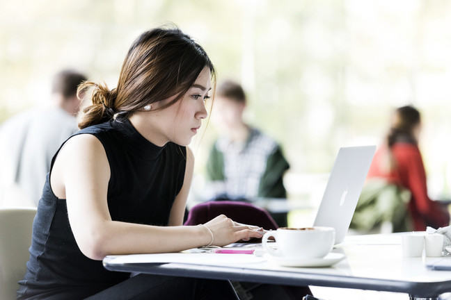 A learner using a laptop keyboard while drinking a cup of coffee