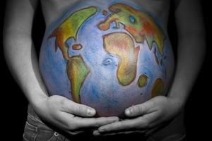 A heavily pregnant woman holds her stomach, which is painted with a map of the world