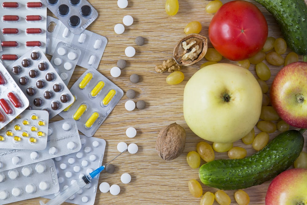 On one side some packets of medicine. On the other side a selection of fruits and vegetables.