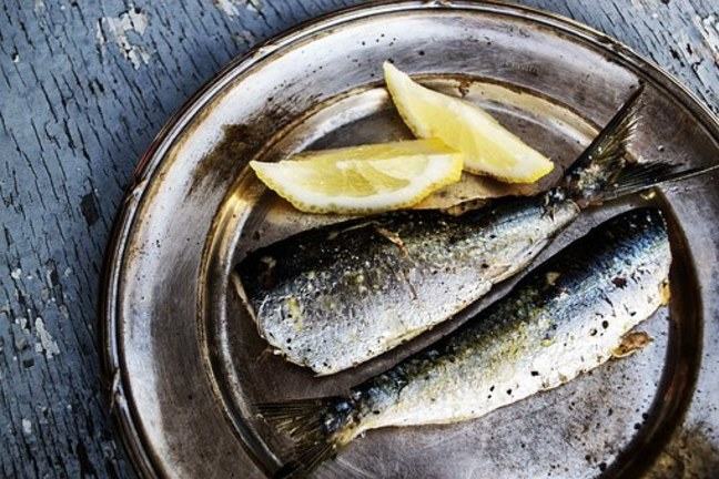 Two cooked fish on a metal plate with two lemon wedges