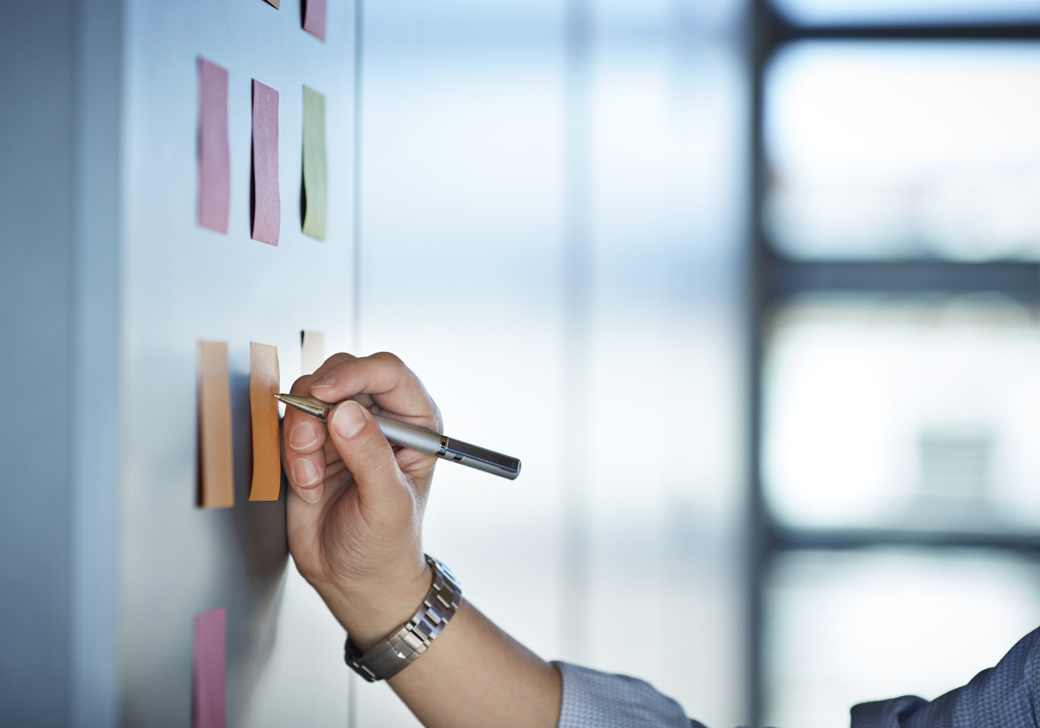 Hand writing on colourful Post-It notes on wall