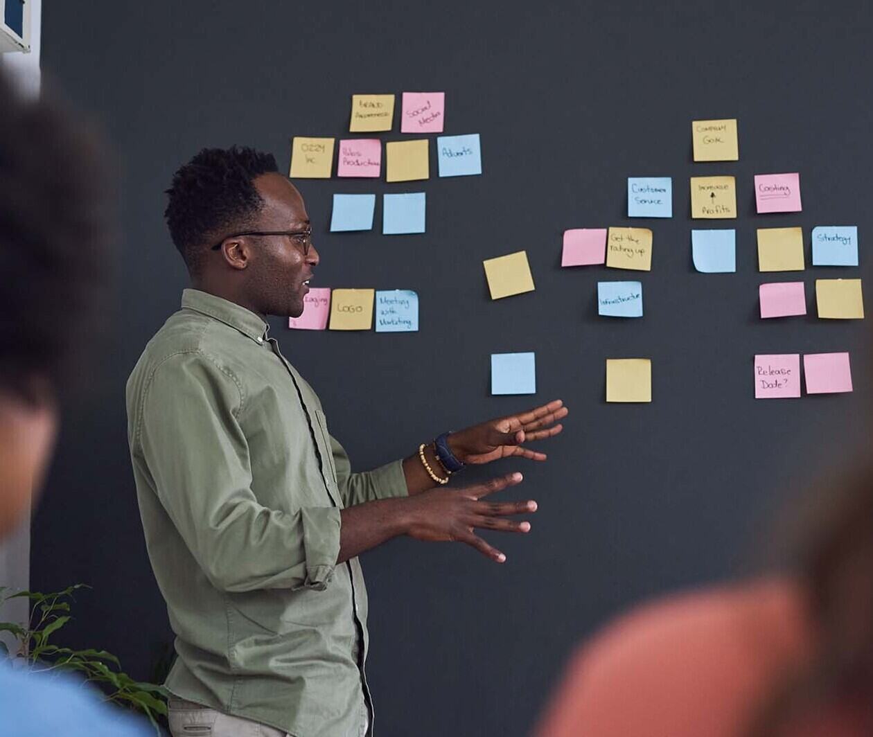 A man in a green shirt stands next to a dark wall full of colourful post-it notes.