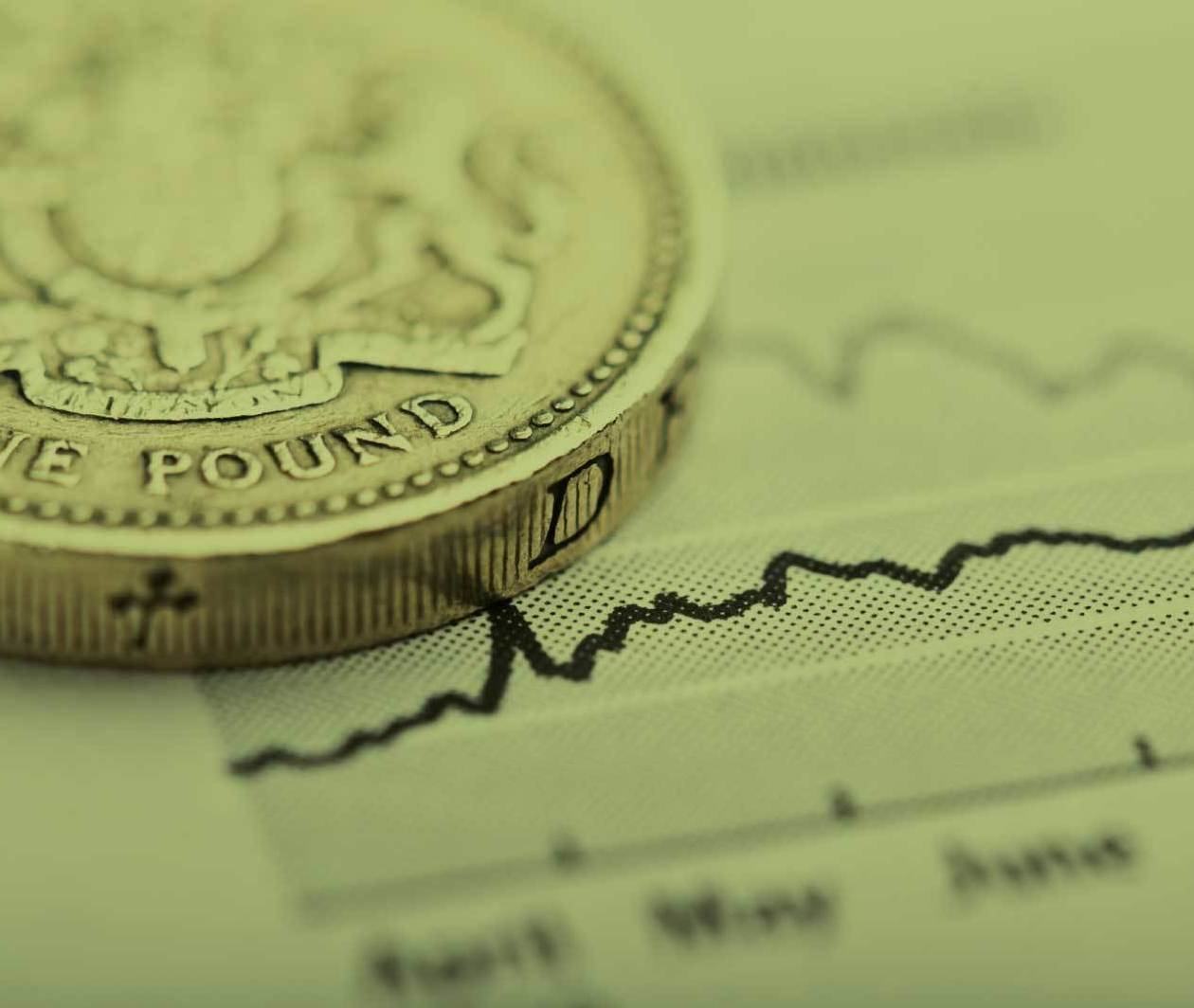 A coin sits on top of a line graph on a piece of paper – a metaphor for financial investments