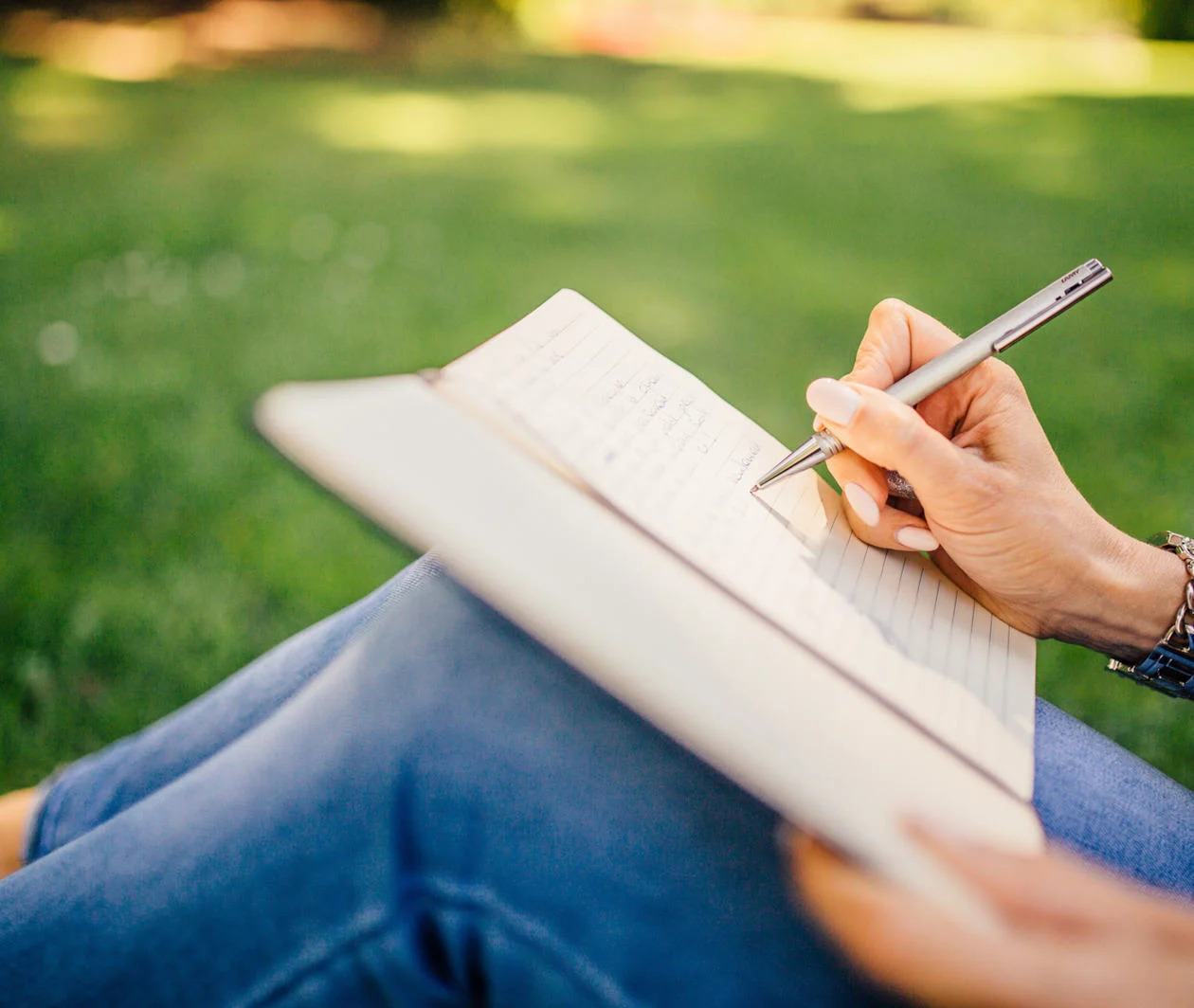 Person sitting on the grass writing in a notebook