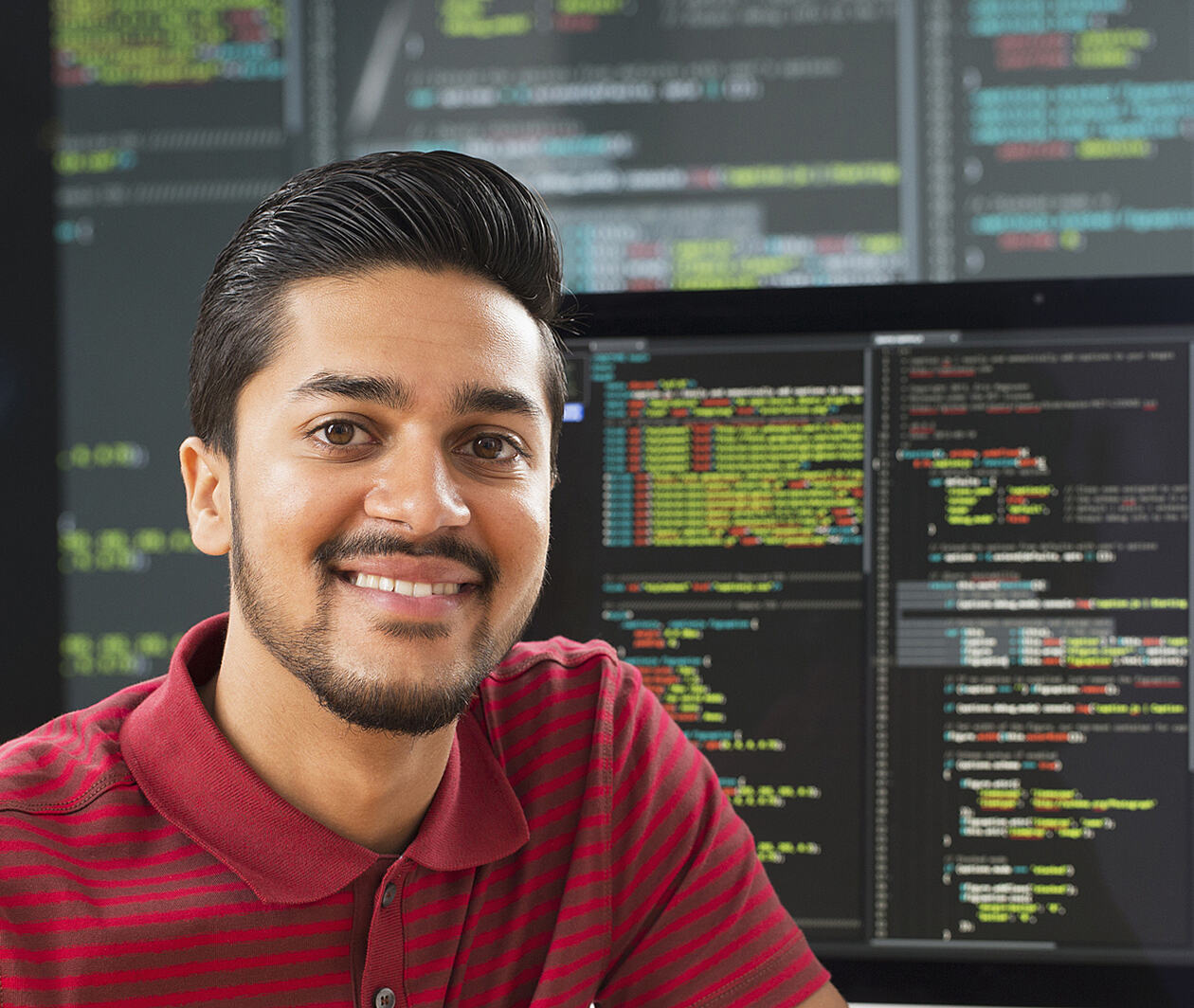 Man smiling at the camera in front of black screens of code.