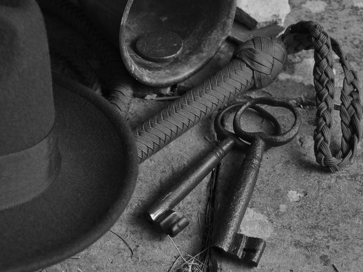 Fedora hat, bullwhip, rusty keys and coin in a leather cup on a concrete floor