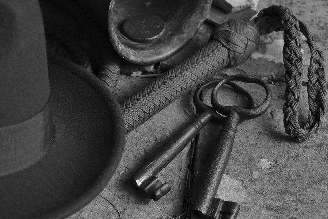 Fedora hat, bullwhip, rusty keys and coin in a leather cup on a concrete floor