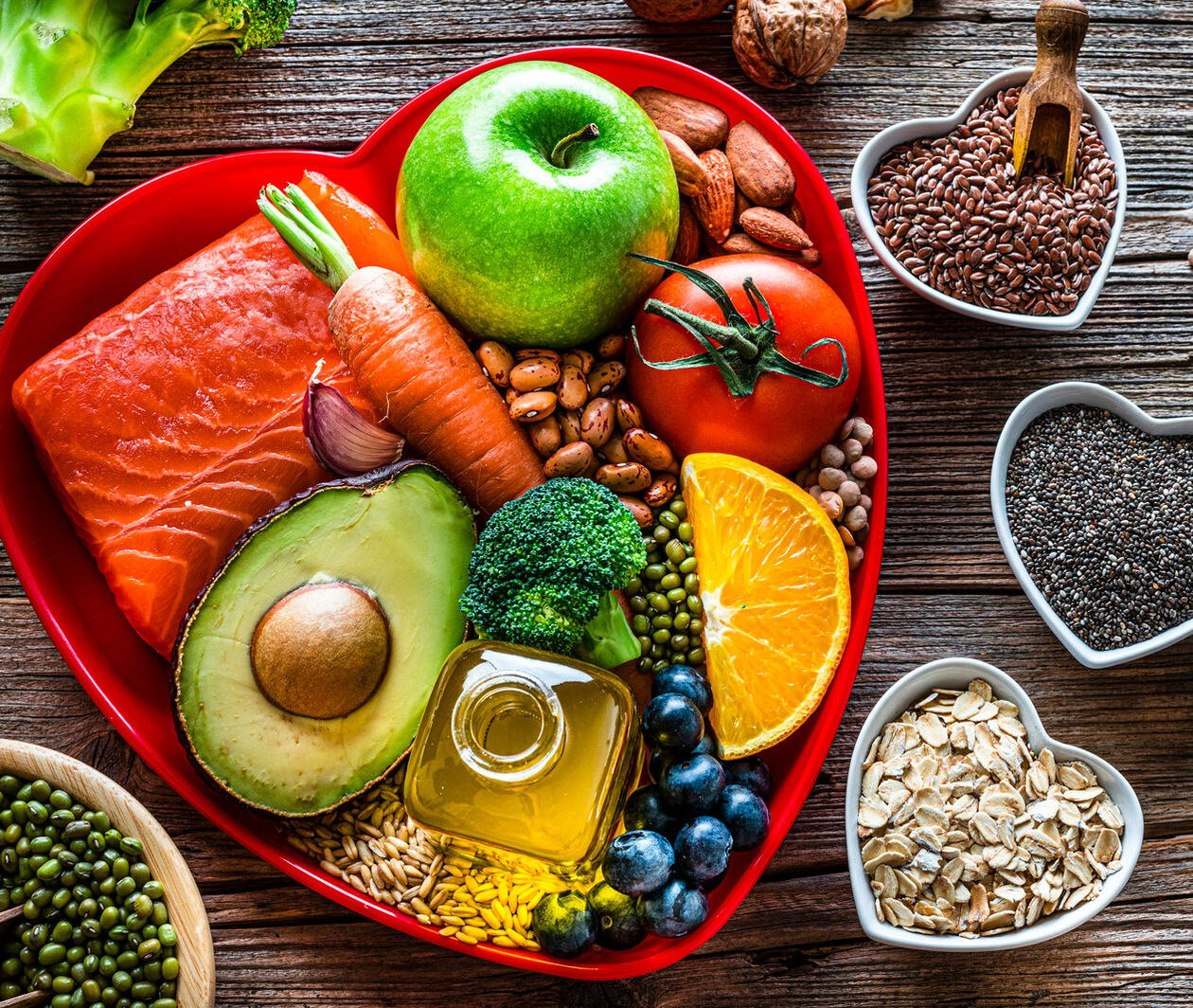 Healthy eating: group of fresh multicolored foods to help lower cholesterol levels and for heart care shot on wooden table. The composition includes oily fish like salmon. Beans like Pinto beans and brown lentils. Vegetables like garlic, avocado, broccoli