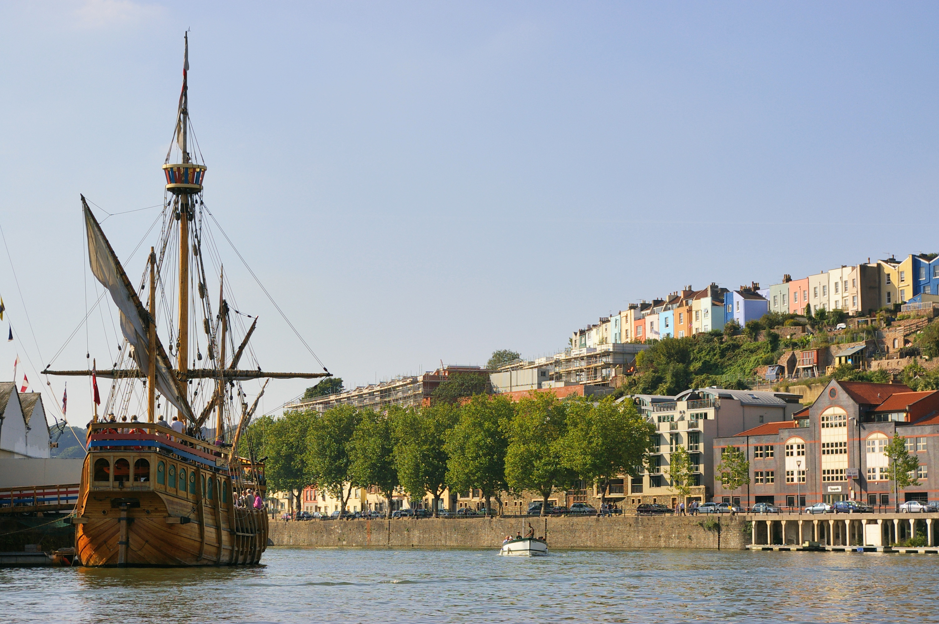 The ship The Matthew moored on the Avon with brightly coloured houses on the skyline.