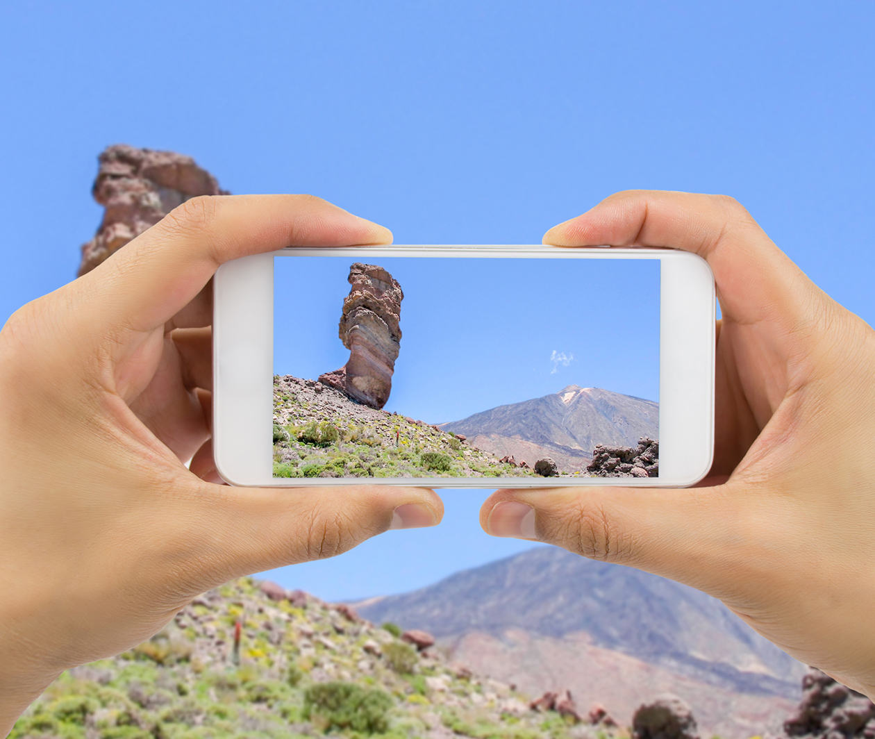 A person holds a smartphone up to take a picture of a landscape – a representation of geology